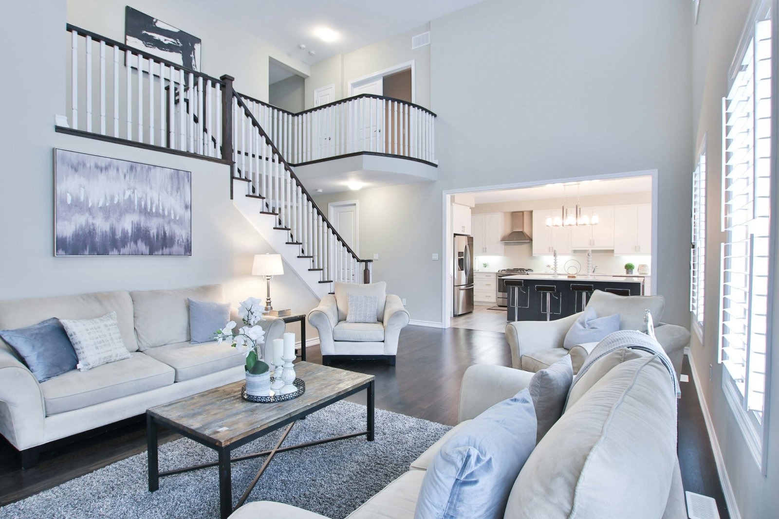 Photo of decluttered home from living room perspective viewing second level and kitchen, colors are white, grey, and blue